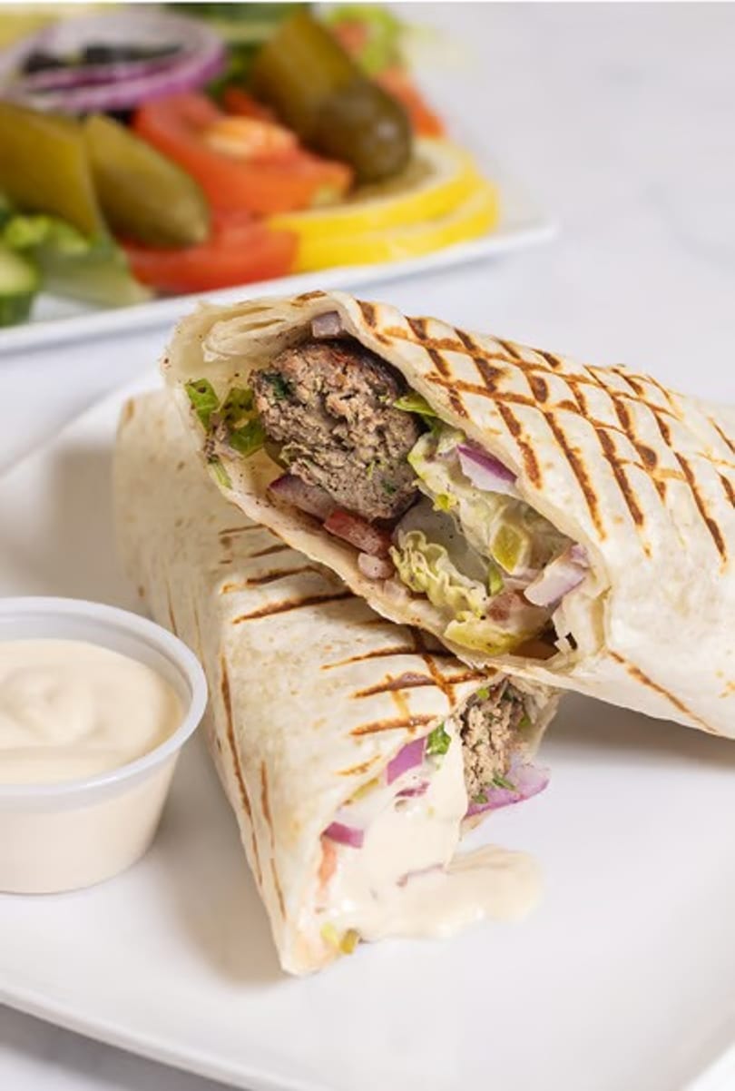 Two grilled wraps filled with meat, lettuce, and red onion, with a side of sauce and salad.